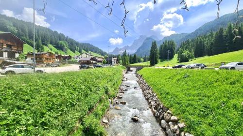a river in the middle of a green field with cars at Hotel B&B Lorenzini Ski in Selva di Cadore