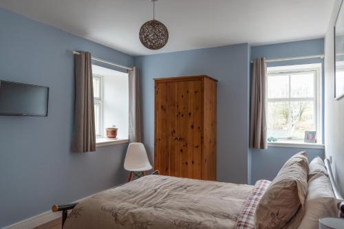 a blue bedroom with a bed and two windows at Altquhur Byre in Drymen