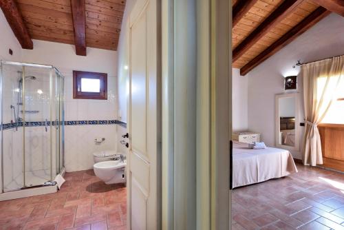 a bathroom with a shower and a toilet and a bed at Hotel S'Abba e Sa Murta in Tortolì