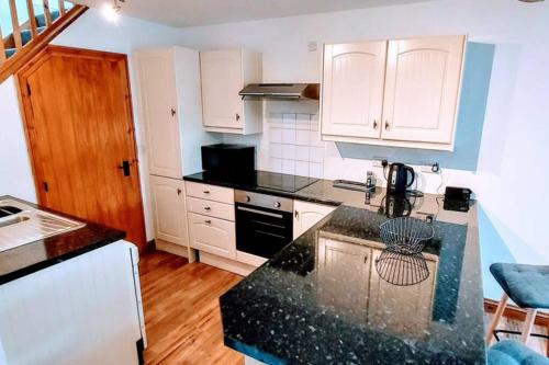 cocina con armarios blancos y encimera negra en Town centre cottage, en Tewkesbury