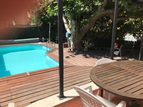 eine Holzterrasse mit einem Tisch und einem Pool in der Unterkunft Chambre climatisée avec sdb privée dans une villa avec piscine ouverte d'avril à mi octobre in Marseille