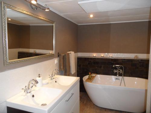 uma casa de banho com 2 lavatórios, uma banheira e um espelho. em B&B Manderscheid-Blick em Pantenburg