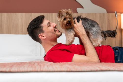 a man laying on a bed with a dog on his back at Mercure Itajai Navegantes in Itajaí