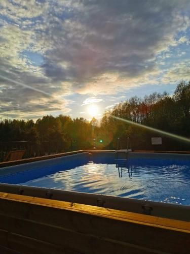 a large swimming pool with the sun in the background at Forest House - Domy Mazur in Regiel