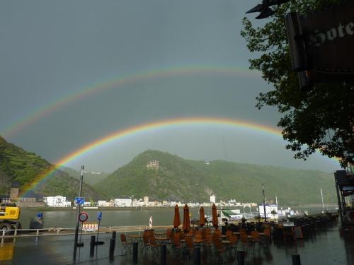 a rainbow over a body of water with tables and chairs at Hotel am Markt Sankt Goar in Sankt Goar
