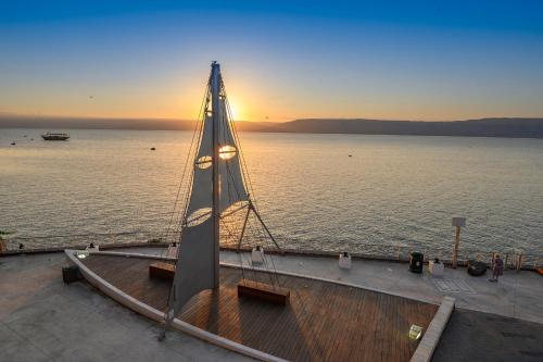 a boat with a sail on the water at sunset at Shirat Hayam Boutique Hotel in Tiberias