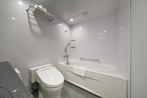 a white bathroom with a toilet and a bath tub at MUSTARD HOTEL SHIMOKITAZAWA in Tokyo