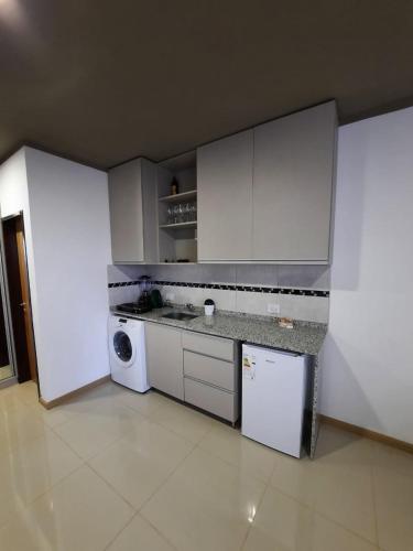 cocina con armarios blancos, lavadora y secadora en Monoambiente céntrico en Posadas