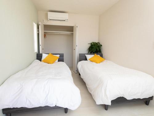 two beds in a room with white and yellow pillows at Ｖｉｌｌａ・Ｃｈａｒｍｅ in Motobu
