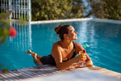 a woman sitting next to a swimming pool with a drink at Beyaz Yunus Hotel - Adult Only in Oludeniz