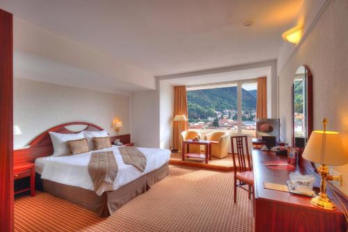 ブラショヴにあるホテル アロ パレスのベッド、デスク、窓が備わるホテルルームです。