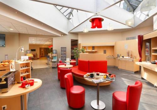 a lobby with red chairs and tables and a kitchen at Ibis Le Havre Sud Harfleur in Port de Harfleur
