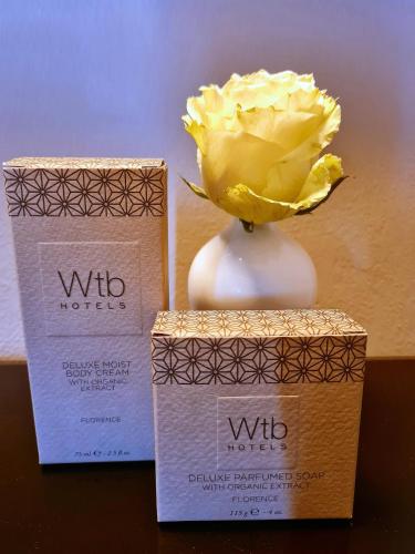 a yellow rose in a white vase next to two boxes at Santa Maria Novella - WTB Hotels in Florence