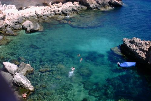 a group of people swimming in the water near rocks at Apulia Bed&Breakfast in Mattinata