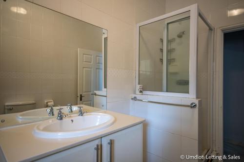 a white bathroom with a sink and a mirror at Wavecrest in Umdloti
