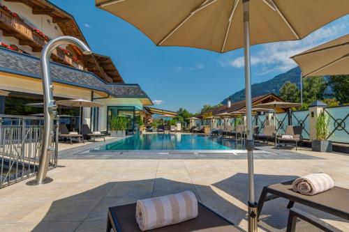 a pool at a resort with chairs and an umbrella at Hotel Post in Kaltenbach