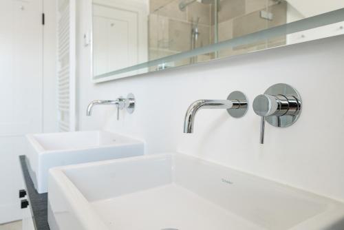 a white bathroom with two sinks and two faucets at Loddis Hüs in Wenningstedt