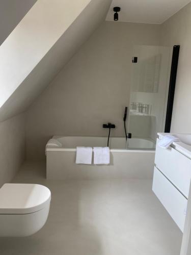 a white bathroom with a toilet and a bath tub at Les Cigognes in Knokke