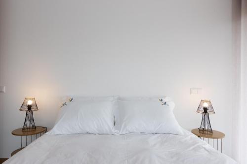a bed with white sheets and two lamps at Abraços dos Avós - Casas de aldeia in Viana do Castelo