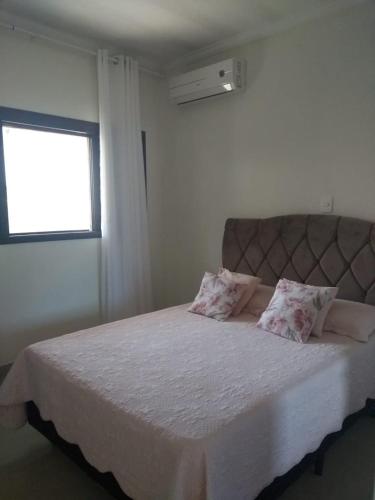 a bedroom with a bed with white sheets and a window at Vila do Aconchego in Ubatuba