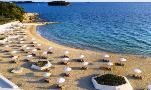 a sandy beach with umbrellas and the ocean at EXCELSIOR Apartments Rovinj in Rovinj
