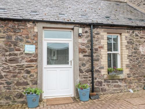 a stone cottage with a white door and two potted plants at Adams House in Eyemouth