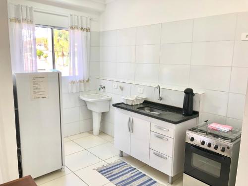 a white kitchen with a sink and a refrigerator at Novo Porto- Apartamentos 2 quartos, varanda, cozinha integrada in Piracicaba