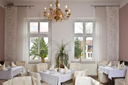 un restaurante con mesas y sillas blancas y ventanas en Hotel Adler, en Greifswald