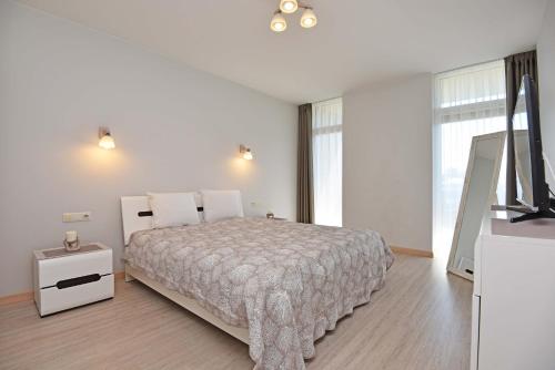 a white bedroom with a bed and a television at Ritos Apartamentai Palangoje in Palanga