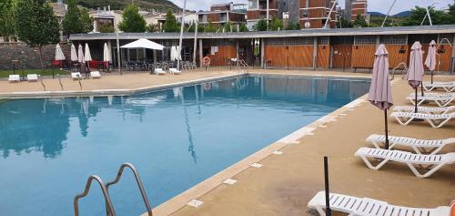 a large swimming pool with chairs and umbrellas at APARTAMENTO PIRINEO DE HUESCA, JACA, FORMIGAL, PANTICOSA in Sabiñánigo