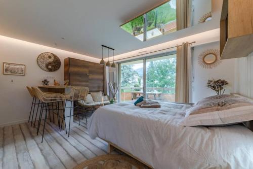 a bedroom with a bed and a table and a window at LE QUINTESSENCE: Balnéo & Luminothérapie + parking in Voiron