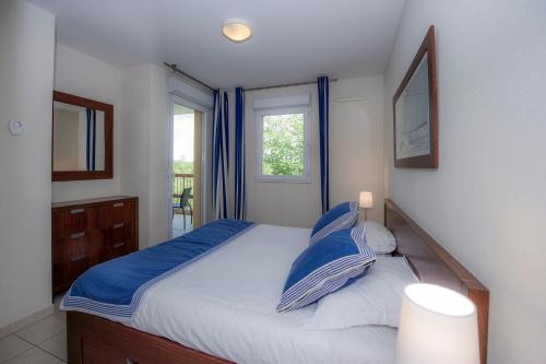 a bedroom with a bed with blue pillows and a window at Goélia Mandelieu Riviera Resort in Mandelieu-la-Napoule