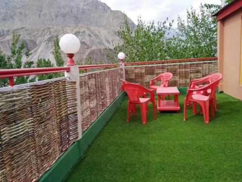 a balcony with red chairs and a table on the grass at High Cliff Guest House in Khaplu