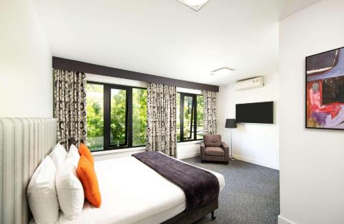 a bedroom with a bed and a chair and windows at Comfort Hotel East Melbourne in Melbourne