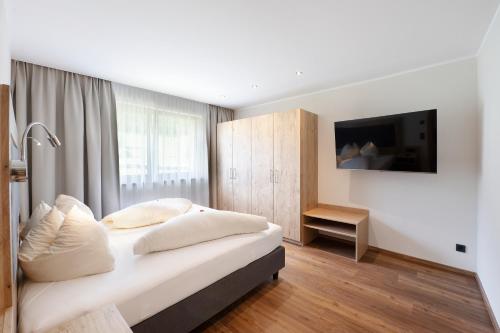 a bedroom with a bed with white pillows and a television at Golf- und Sporthotel Moarhof in Walchsee