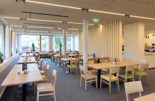 un restaurante con mesas y sillas de madera y ventanas en JUFA Hotel Laterns - Klangholzhus, en Laterns