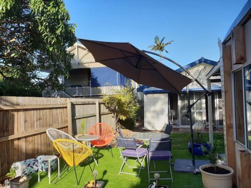 a backyard with a table and chairs and an umbrella at WOODY Pt - AMAZING 1970's SHARE HOUSE BY THE SEA-4 rooms available! in Woody Point