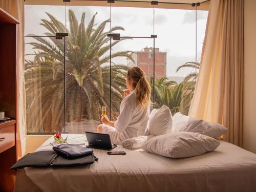 a woman sitting on a bed looking out a window at HOTEL AVENIDA in Tacna