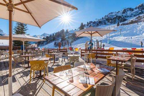 a restaurant with tables and umbrellas in the snow at Hotel Les Arolles in Méribel
