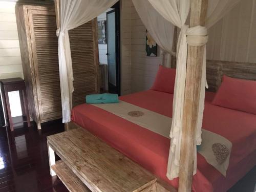 a bedroom with a bed with red sheets and a canopy at La Perle Tahaa in Tapu' amu