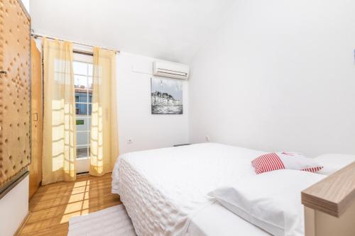 a white bedroom with two beds and a window at Apartmani Nadia in Punat