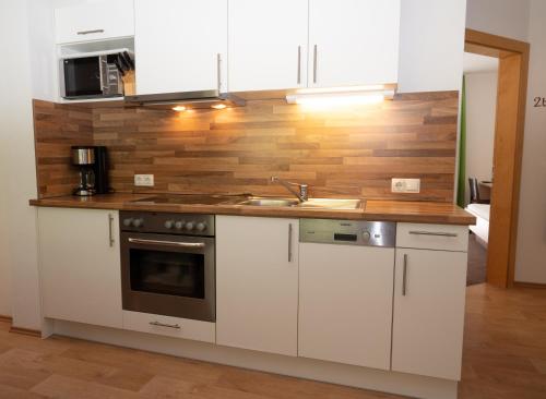 a kitchen with white cabinets and a wooden wall at Apart welcom in Ischgl