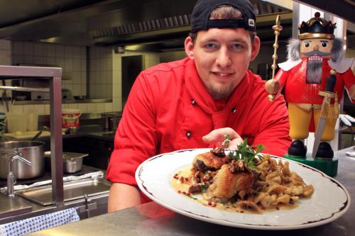a man in a kitchen holding a plate of food at Hotel Erbgericht Buntes Haus in Seiffen