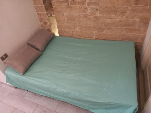 a green bed in a room with a brick wall at Le dimore di Talos Argonauti in Ruvo di Puglia