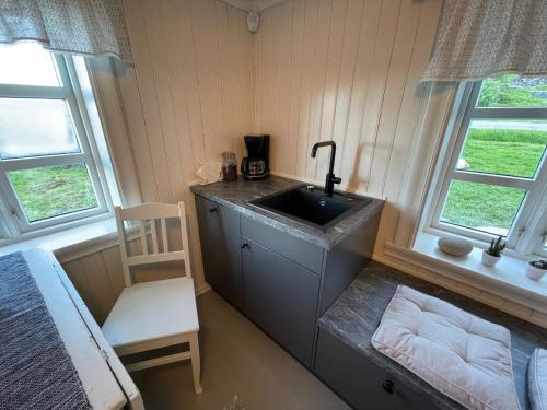 a kitchen with a sink and a chair and two windows at Storhella - Feriehus med fantastisk beliggenhet in Sennesvik