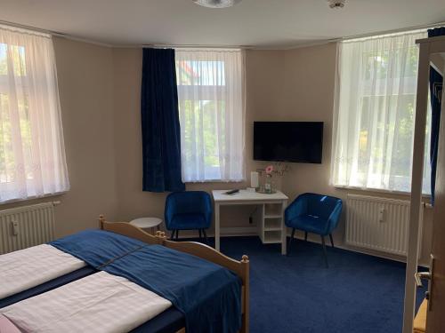 a bedroom with a bed and a desk with two blue chairs at Pension Triebischtal in Meißen