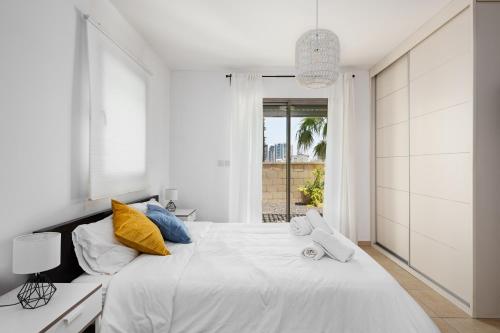 a white bedroom with a large bed with yellow and blue pillows at Water Front Blue Lguna Garden Apartment 2bd in Herzliya B