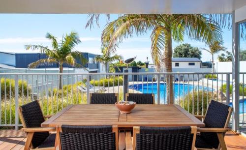 a wooden table and chairs on a balcony with a pool at Ohope Beach Resort in Ohope Beach