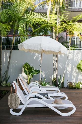 a group of white lounge chairs and an umbrella at Noosa Heads Motel in Noosa Heads