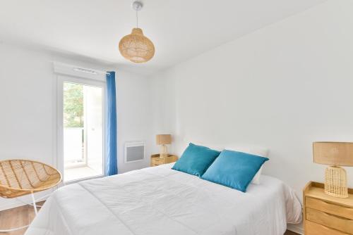 un lit blanc avec des oreillers bleus dans une chambre dans l'établissement Confort et bel appartement au coeur de Lacanau, à Lacanau